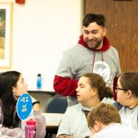 A student smiles while walking past a round table full of other students